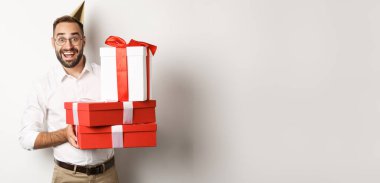 Tatiller ve kutlamalar. Mutlu adam doğum gününde hediyeler alıyor, hediyeler alıyor ve heyecanlı görünüyor, beyaz arka planda duruyor..