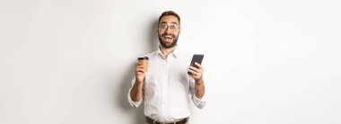 Harika bir iş adamı kahve içiyor, cep telefonuyla harika bir online teklif yapıyor, beyaz arka planda duruyor..