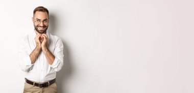 Genç kurnaz işadamı parmaklarını çırpıyor ve gülümsüyor. Sinsi, entrikacı plan, beyaz arka planda duruyor..