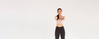 Gülümseyen, yakışıklı ve ince Asyalı fitness koçu aktif giyimli bayan sporcu egzersiz ekipmanları gösteriyor, direnç bandı tutuyor, egzersiz yapıyor, beyaz arka plan.