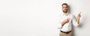 Şüpheli ve endişeli bir adam kararsız görünüyor, sağ üst köşeyi işaret ediyor tereddütlü, beyaz arka planda duruyor..