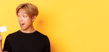 Afallamış Asyalı adamın kredi kartından bahseden yakın plan fotoğrafı, sarı arka planda duruyor..