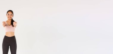 Gülümseyen, yakışıklı ve ince Asyalı fitness koçu aktif giyimli bayan sporcu egzersiz ekipmanları gösteriyor, direnç bandı tutuyor, egzersiz yapıyor, beyaz arka plan.