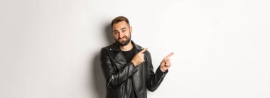 Deri ceketli, kuşkucu ve hayal kırıklığına uğramış bir adam, sol üst köşeyi işaret ediyor, kötü promosyon teklifini gösteriyor, beyaz arka planda isteksiz duruyor..