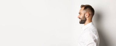 Yakışıklı sakallı adamın, sola bakıp gülümseyen, beyaz arka planda duran yakın plan fotoğrafı..