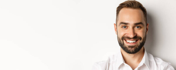 Headshot of handsome bearded man smiling, standing against white background.