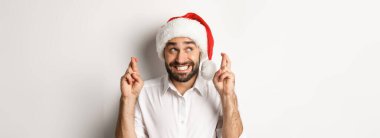 Parti, kış tatili ve kutlama konsepti. Noel Baba şapkalı mutlu bir adam Noel dileği diliyor, şans diliyor ve gülümsüyor heyecanlı, beyaz bir geçmişi var..