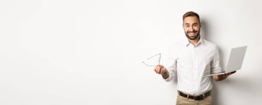 Profesyonel özgüvenli iş adamı laptopta işini yapıyor, tatmin olmuş görünüyor, beyaz arka planda duruyor..