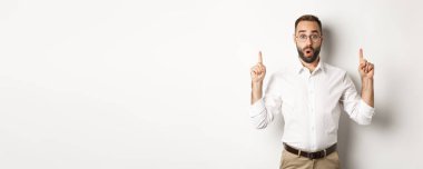 Gözlüklü, heyecanlı yakışıklı adam, işaret ediyor, bilgi afişi gösteriyor, beyaz arka planda duruyor. Boşluğu kopyala