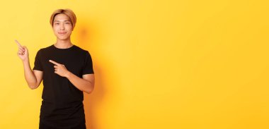 Siyah tişörtlü, gülümseyen yakışıklı Asyalı adamın portresi sol üst köşeyi işaret ediyor, logo ya da afiş gösteriyor, sarı arka plan.