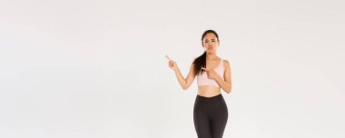Şüpheci, hayal kırıklığına uğramış Asyalı fitness kızı, sporcu kadın sırıtarak ve somurtarak kötü spor salonundan ya da berbat spor aletlerinden şikayet ederken, sağ üst köşeden memnuniyetsiz, beyaz arka plan.