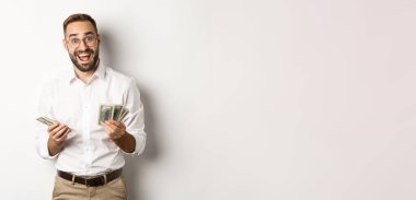 Yakışıklı iş adamı para sayarken heyecanlı görünüyor, beyaz arka planda duruyor..