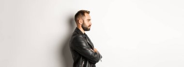 Deri ceketli yakışıklı, ciddi bir adamın profili, sola bakıyor, göğsüne bakıyor özgüvenli, beyaz arka planda..