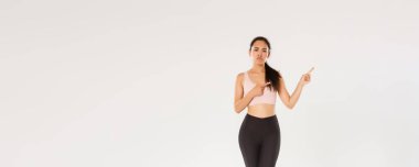 Şüpheci, hayal kırıklığına uğramış Asyalı fitness kızı, sporcu kadın sırıtarak ve somurtarak kötü spor salonundan ya da berbat spor aletlerinden şikayet ederken, sağ üst köşeden memnuniyetsiz, beyaz arka plan.