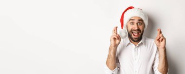 Parti, kış tatili ve kutlama konsepti. Noel Baba şapkalı mutlu adam Noel dileği diliyor, şans diliyor ve heyecanlı görünüyor, beyaz arka plan.