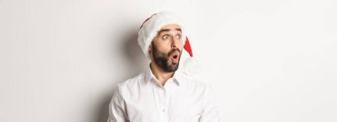 Noel Baba şapkalı şaşkın sakallı adamın yakın çekimi, şaşırmış bir yüz, yılbaşı promosyon teklifi, beyaz arka planda duran.