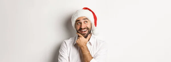 パーティー 冬の休日やお祝いの概念 幸せな男のクローズアップクリスマスギフトリストを計画し サンタの帽子を身に着けて 左上隅を思慮深く見て 白い背景 — ストック写真
