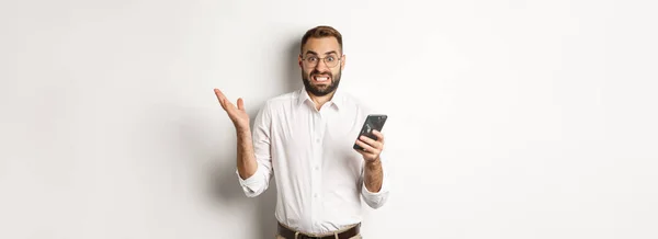 携帯電話で奇妙なメッセージを読んでいるビジネスマンを混乱させ いらいらさせ 白い背景の上に立って — ストック写真