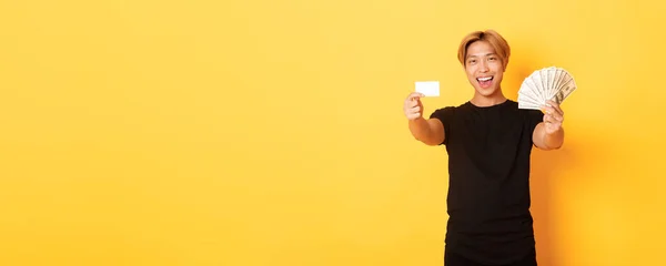 幸せな良い黒のカジュアルな服のアジアの男 お金とクレジットカードを示す 笑顔のお尻 黄色の背景 — ストック写真