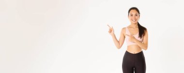Spor, refah ve aktif yaşam tarzı konsepti. Gülümseyen ince ve tatlı Asyalı fitness kızı, sol üst köşeyi gösteren bayan sporcu, spor malzemeleri satış promosyonu veya spor salonu teklifini gösteriyor..