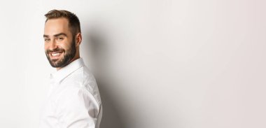 Kendine güvenen iş adamının yakın çekimi kameraya yüzünü döner, kendinden emin gülümser, beyaz arka planda durur..