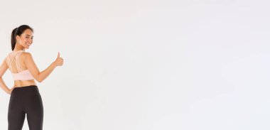 Motive olmuş ve tatmin olmuş Asyalı kadın koç, spor giyim atleti kız kameraya baş parmağını kaldırıp, üretkenlik eğitimine hazır, beyaz arka plan.