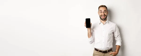スマートフォンの画面アプリを示す素晴らしいハンサムなビジネスマン 白い背景の上に立って — ストック写真