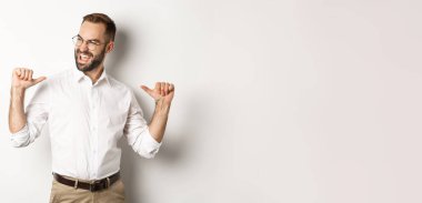 Tatmin olmuş ve kendinden emin iş adamı kendini işaret ederek beyaz arka planda duruyor..