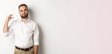 Hayal kırıklığına uğramış erkek girişimci küçük bir nesne gösteriyor ve iç çekiyor, beyaz arka planda duruyor..