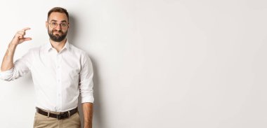 Memnun olmayan sakallı iş adamı, küçük bir jest yapıyor, hayal kırıklığına uğramış görünüyor, beyaz arka plana karşı duruyor..