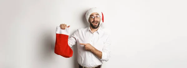 メリークリスマス休暇のコンセプト 幸せな大人男受信ギフトでXmasソックス 見て興奮 身に着けているサンタ帽子 白の背景 — ストック写真