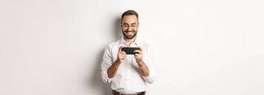 Mutlu iş adamı cep telefonundan video izliyor, beyaz arka planda duruyor..