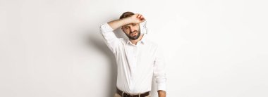 Yorgun ofis çalışanı kalkış gözlüğü, alnındaki teri koluyla siliyor, beyaz arka planda kurumuş bir şekilde duruyor..