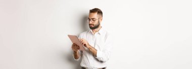 İşadamı dijital tablet üzerinde çalışıyor, meşgul görünüyor, beyaz arka planda duruyor..