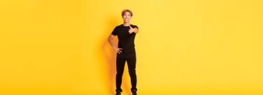 Uzun boylu, yakışıklı, sarı saçlı, el sıkışmak için elini uzatan, sarı arka planda duran Koreli bir adam..