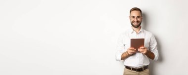 Gözlüklü yakışıklı adam dijital tablet kullanıyor, gülümsüyor, beyaz arka plana karşı duruyor..