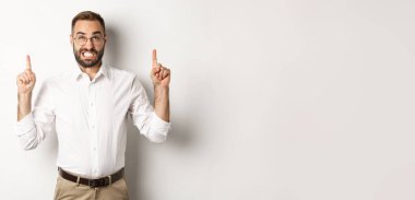 Şüpheci ve endişeli adam yukarı bakıyor ve işaret ediyor, tereddüt ediyor, beyaz arka planda duruyor..