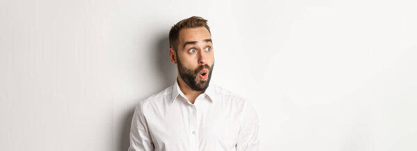 Close-up of happy and surprised man looking left with amazed face, white background.