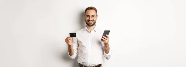 ビジネスとオンライン決済 笑顔の男性起業家ショッピングクレジットカードと携帯電話 白い背景の上に立って — ストック写真