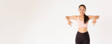 Spor, refah ve aktif yaşam tarzı konsepti. Heyecanlı ve mutlu Asyalı spor giyim kızı, parmakları aşağıda ve büyük indirimlerle şaşkın bakıyor, afiş okuyor, beyaz arka plan.