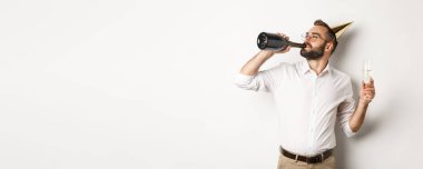 Kutlama ve tatiller. Doğum günü partisinde şişeden şampanya içen adam beyaz arka planda duruyor..