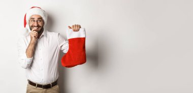 Mutlu Noeller, tatil konsepti. Yetişkin bir adam mutlu ve meraklı görünüyor, Noel Baba şapkası takıyor, beyaz bir geçmişi var, hediyeler alıyor..