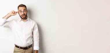 Kafasını işaret eden kafası karışmış bir adam, azarlayan bir çalışan, garip bir şeye tepki veren, beyaz arka planda duran.