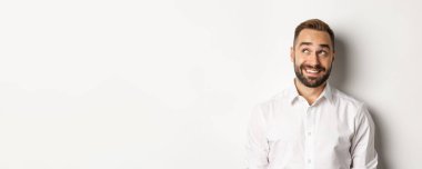 Sakallı yakışıklı adamın yakın çekimi, sol üst köşede düşünceli görünüyor, görüntülüyor ve gülümsüyor, beyaz arka plan.