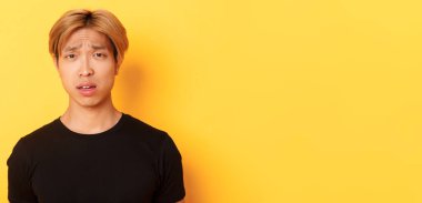 Kafası karışmış, kafası karışmış, kafası karışmış, ağzı açık, suratı asık, sarı arka planda duran Asyalı sarışının yakın çekimi..