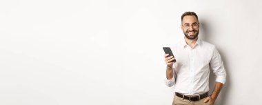 Akıllı telefon kullanan yakışıklı bir yönetici ve gülümsüyor lütfen, mesaj gönderiyor, beyaz arkaplan üzerinde duruyor.
