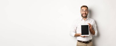 Alışveriş ve teknoloji. Dijital tablet ekranı gösteren düşünceli bir adam, sol üst köşeye bakıyor ve düşünüyor, beyaz arka planda duruyor..