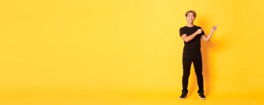 Yakışıklı, kendine güvenen, mutlu gülümseyen, parmaklarını sağa doğru gösteren, logoyu gösteren, sarı arka plan..