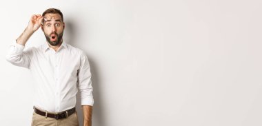 Şaşırmış iş adamı kameraya hayranlıkla bakıyor, beyaz arka planda dikiliyor..