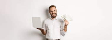 İş ve e-ticaret. Heyecanlı iş adamı elinde dolar ve laptop tutuyor, internette çalışıyor, beyaz arka planda duruyor..